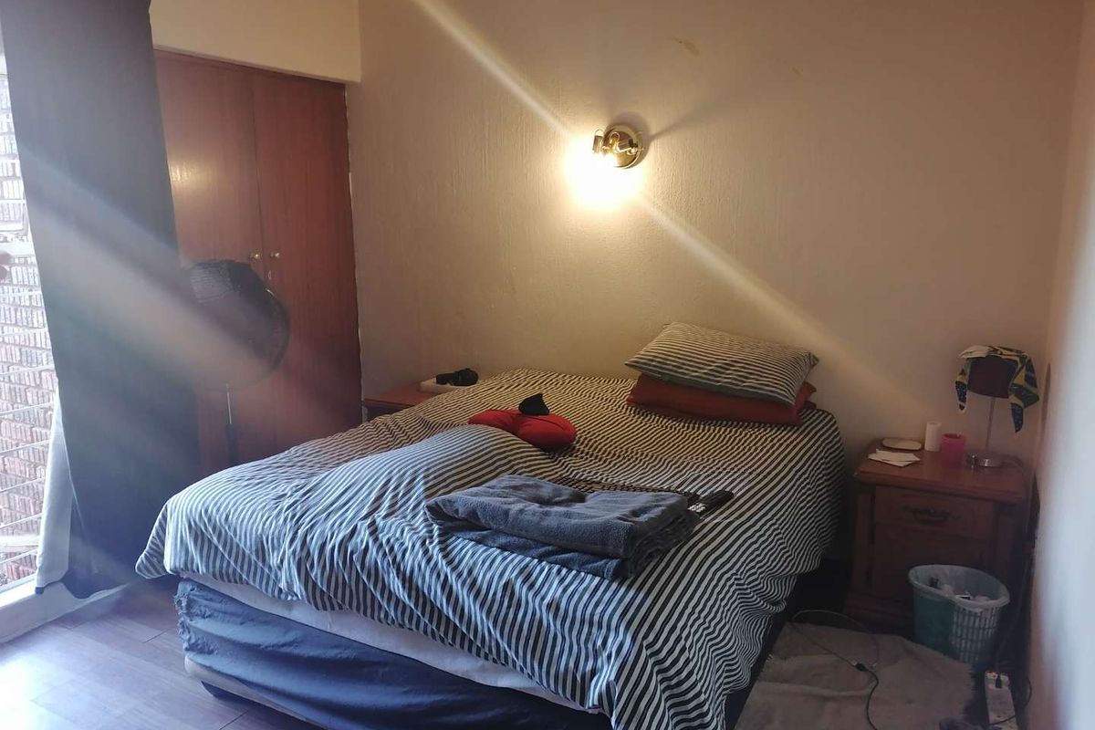 A bedroom featuring laminate flooring, a built-in wardrobe, and a wall-mounted light fixture. The space requires cosmetic updates to improve its overall condition.
