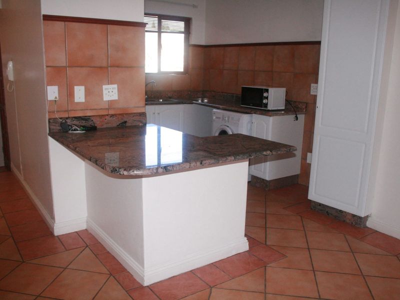 A functional kitchen featuring granite countertops, tiled flooring, and a breakfast bar, offering a practical layout with ample storage space.