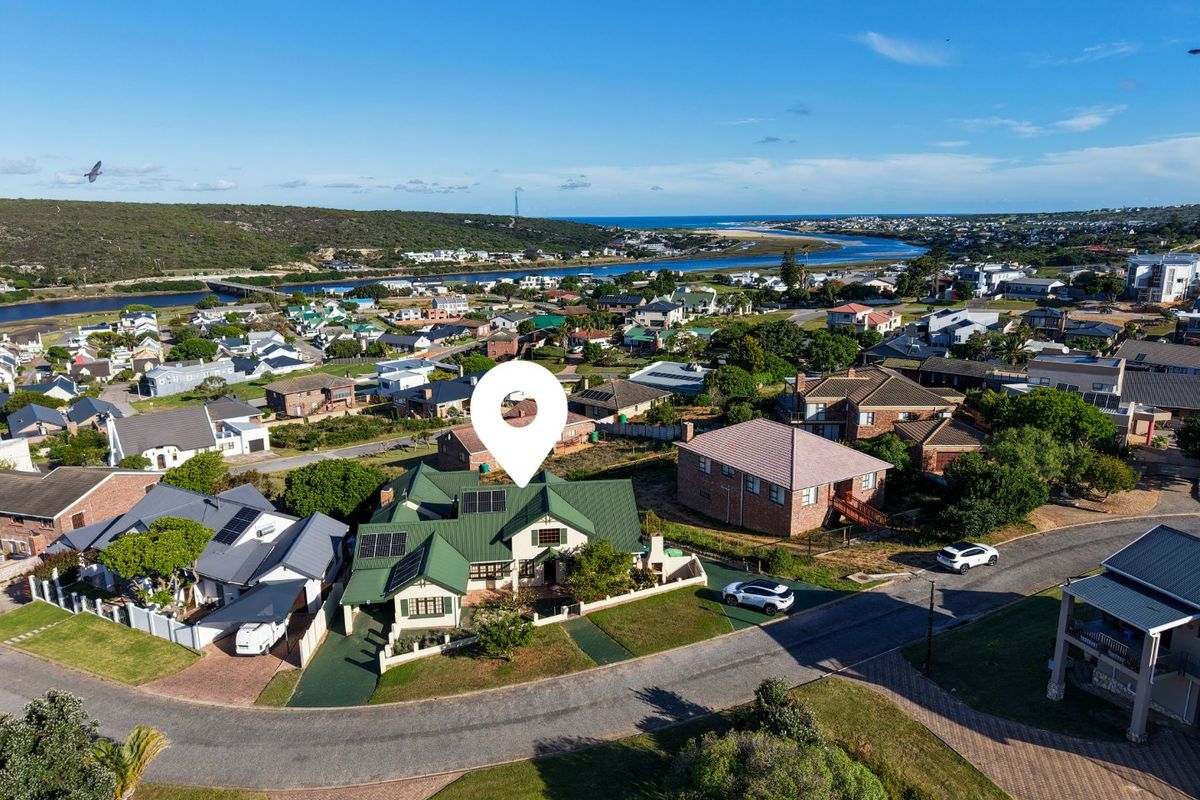Aerial view of the property showcasing the roof structure, solar panels, driveway, and surrounding residential neighborhood with coastal views.