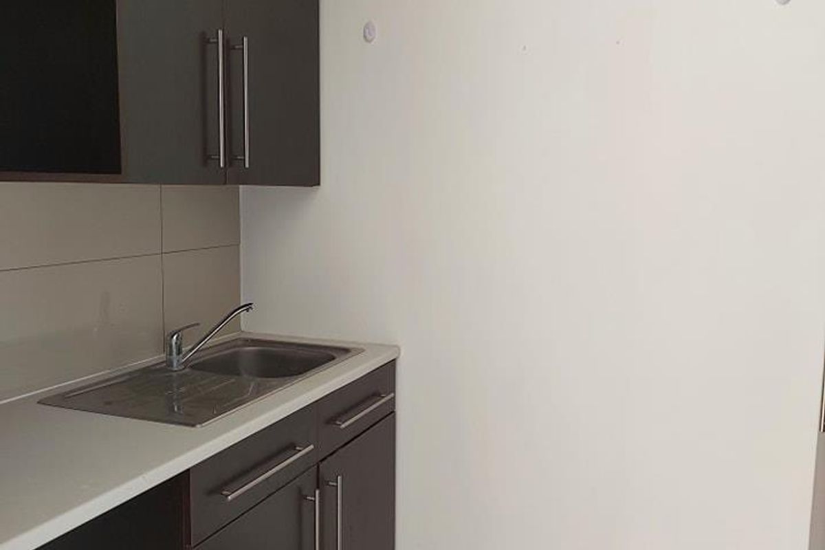 A compact kitchenette area featuring dark cabinetry, a stainless steel sink, and tiled flooring, suitable for office utility use.