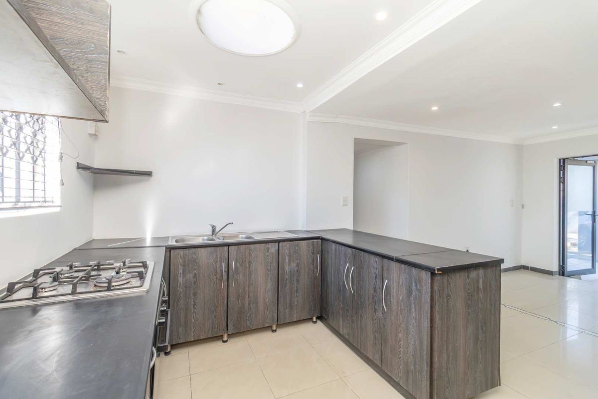 A functional kitchen featuring dark wood-grain cabinetry, a gas hob, double sink, and tiled flooring, illuminated by recessed lighting and a skylight.