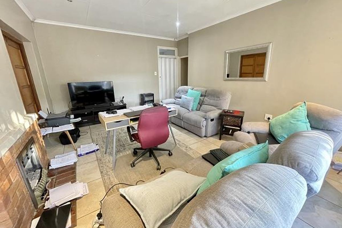 A living room featuring tiled flooring, a brick fireplace, and recessed ceiling lighting, currently utilized as a multi-purpose living and workspace area.