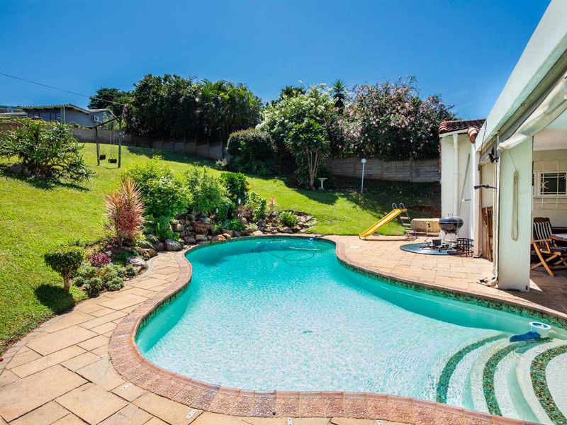 A well-maintained swimming pool area featuring a paved deck, landscaped garden, and a covered patio space, ideal for outdoor relaxation and entertainment.