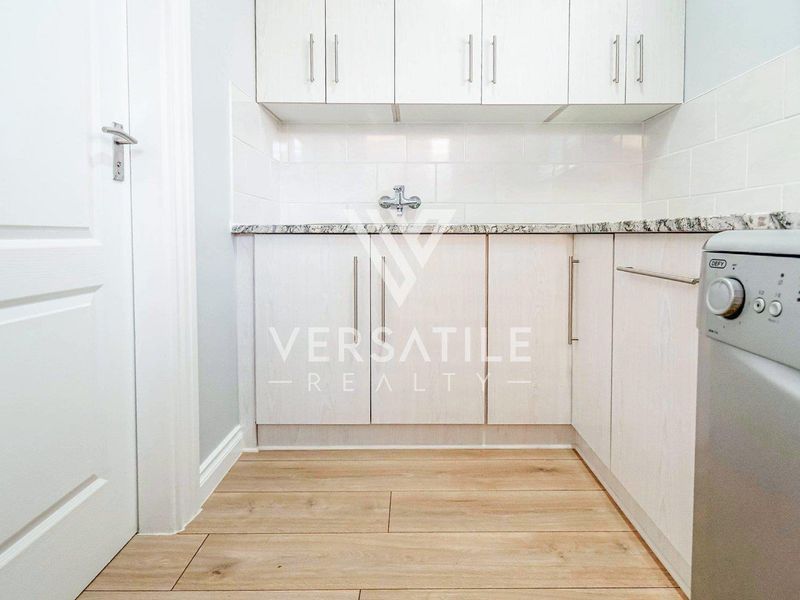 A clean and modern laundry room featuring light wood-finish cabinetry, granite countertops, and a tiled backsplash with durable laminate flooring.