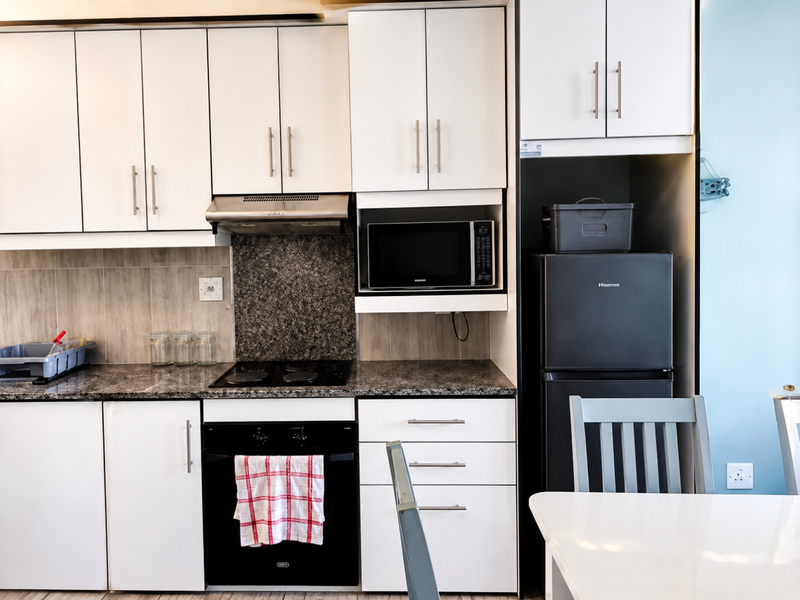 A well-maintained kitchen featuring white cabinetry, granite countertops, a built-in oven, electric hob, and integrated microwave, offering a clean and functional cooking space.