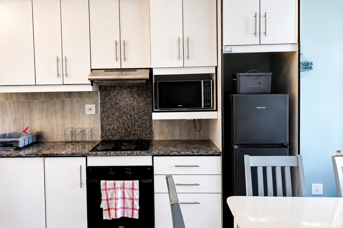 A well-maintained kitchen featuring white cabinetry, granite countertops, a built-in oven, electric hob, and integrated microwave, offering a clean and functional cooking space.
