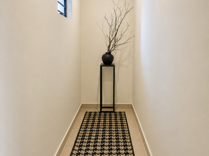 A clean, minimalist hallway featuring neutral walls, tiled flooring, and a small window, providing a bright and well-maintained transition space within the apartment.