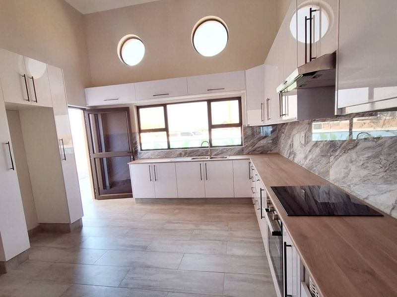 Modern kitchen featuring sleek white cabinetry, marble-effect splashbacks, wooden countertops, integrated appliances, and unique porthole windows, set on neutral porcelain floor tiles.