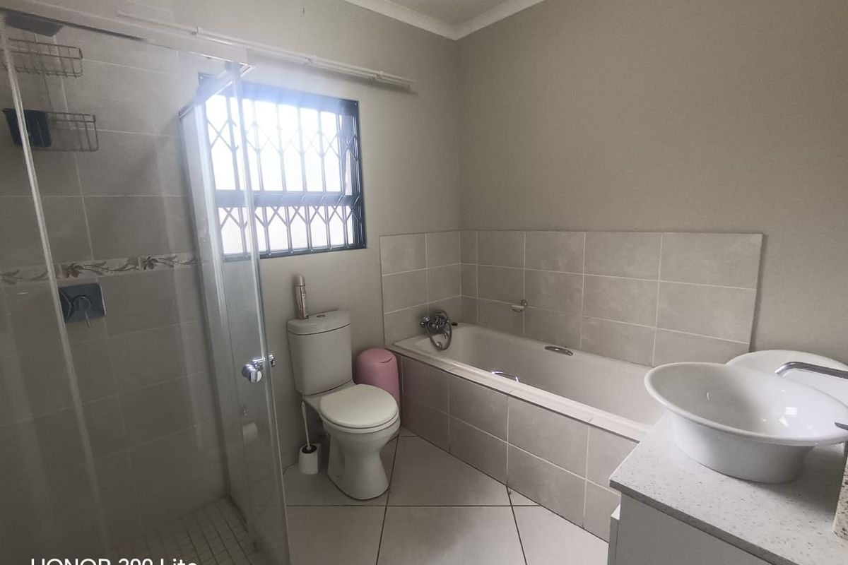 A functional bathroom featuring a built-in bathtub, separate glass-enclosed shower, vanity basin, and toilet with security bars on the window.