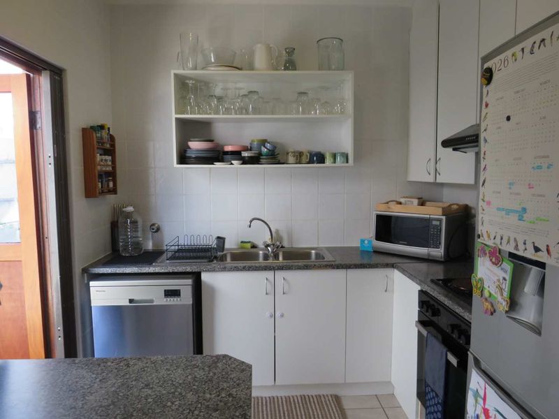 A functional kitchen featuring white cabinetry, laminate countertops, a stainless steel sink, built-in oven, extractor fan, and integrated dishwasher.