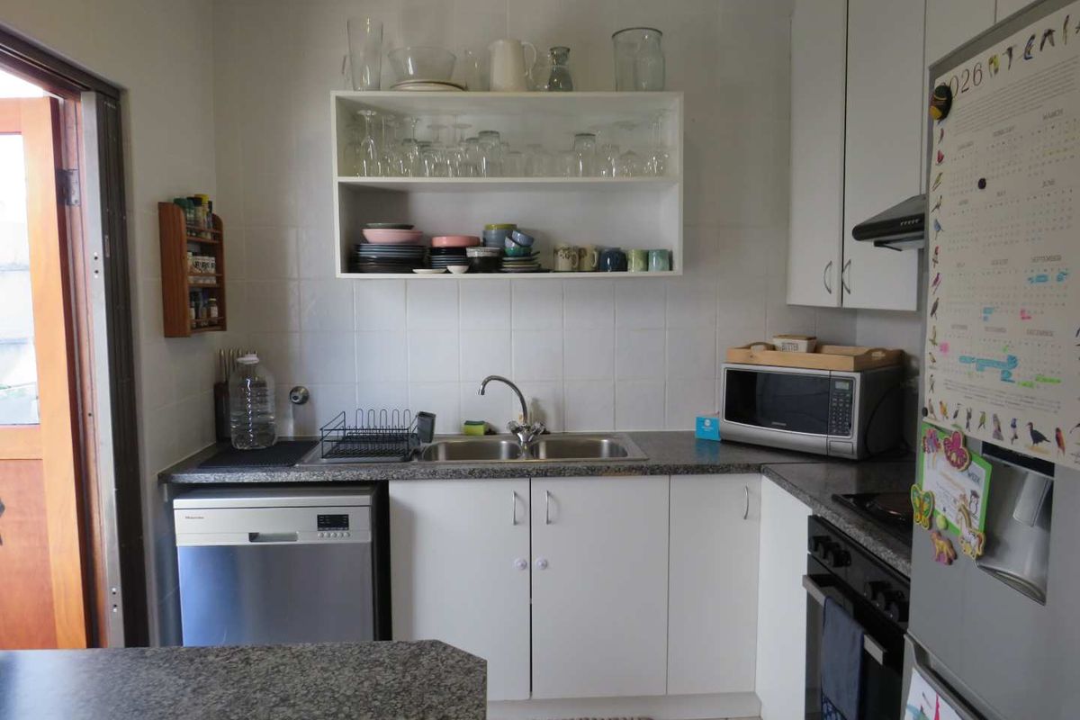 A functional kitchen featuring white cabinetry, laminate countertops, a stainless steel sink, built-in oven, extractor fan, and integrated dishwasher.