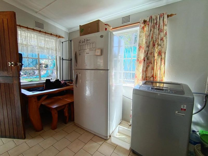 A functional laundry area featuring tiled flooring and security bars on the windows, providing a practical space for utility and washing needs.