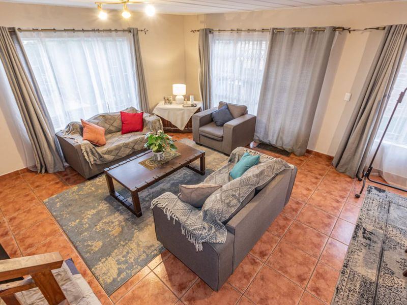 A spacious living room featuring terracotta floor tiles and large windows with curtain rods, offering a bright and comfortable living space.