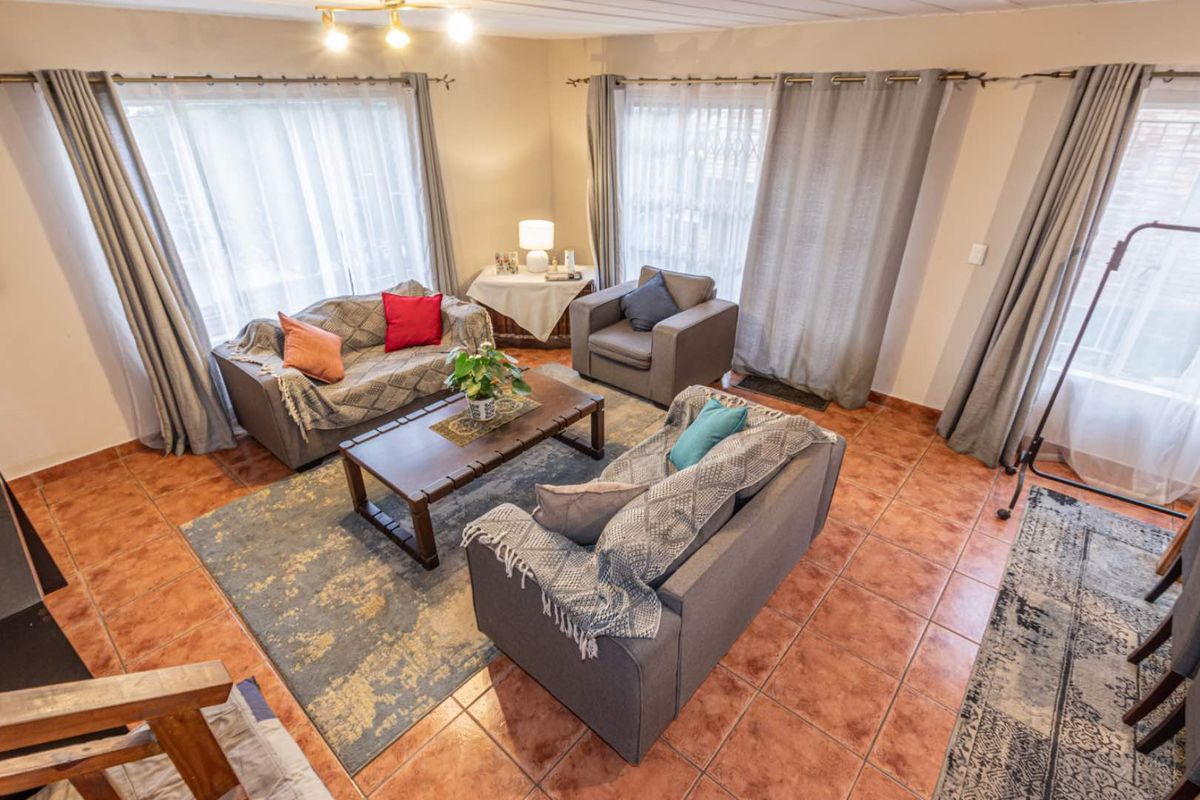 A spacious living room featuring terracotta floor tiles and large windows with curtain rods, offering a bright and comfortable living space.
