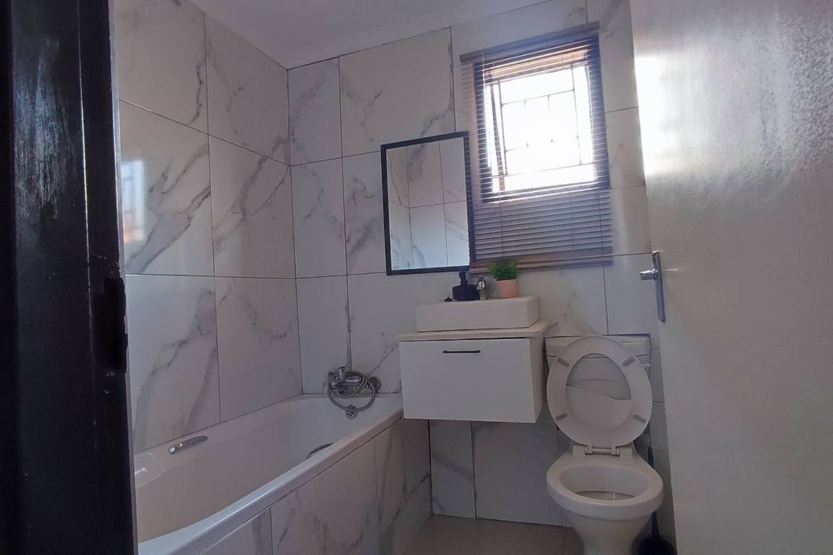 A modern bathroom featuring marble-look wall tiles, a built-in bathtub, a wall-mounted vanity with a vessel sink, and a toilet.
