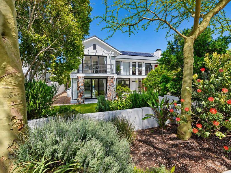 A well-maintained two-story rear facade featuring stone accents, a balcony, and solar panels, set within a lush, landscaped garden.