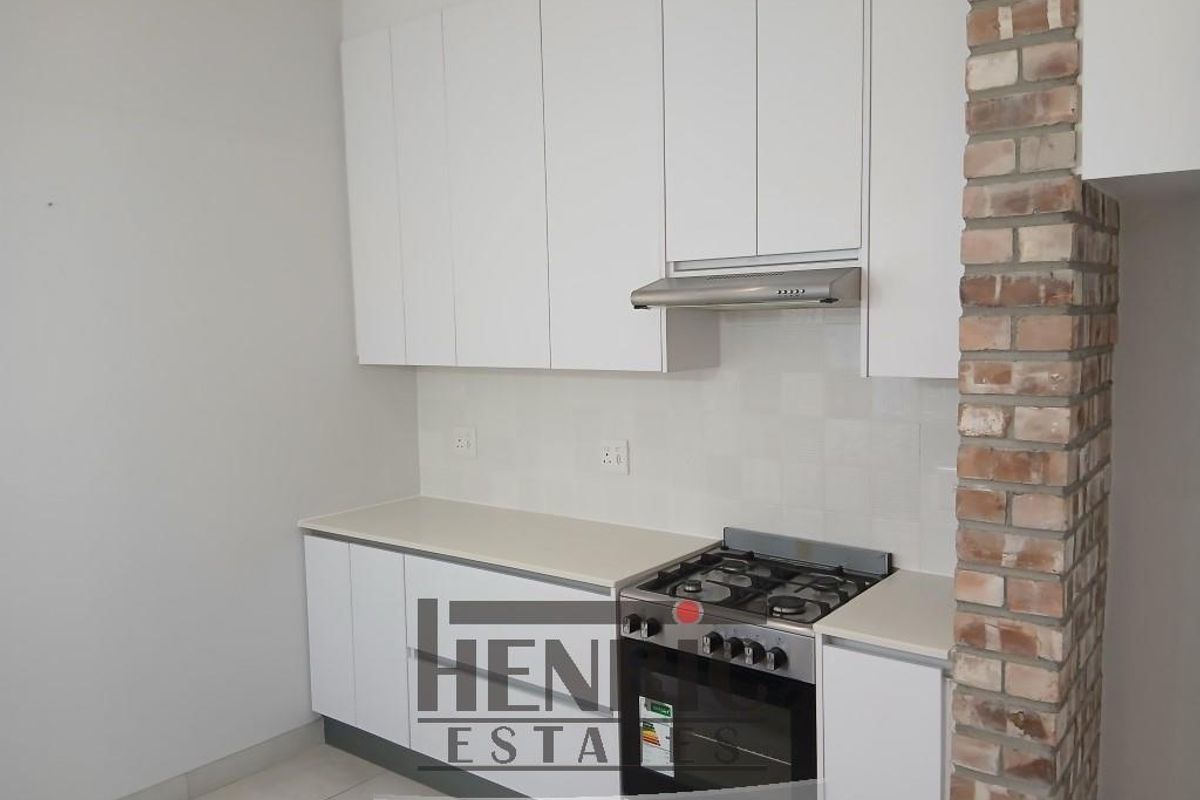 A clean, modern kitchen featuring white cabinetry, a gas stove with an extractor fan, and a decorative exposed brick pillar.