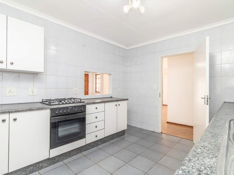 A functional kitchen featuring white cabinetry, granite countertops, a gas hob, oven, and tiled finishes throughout.