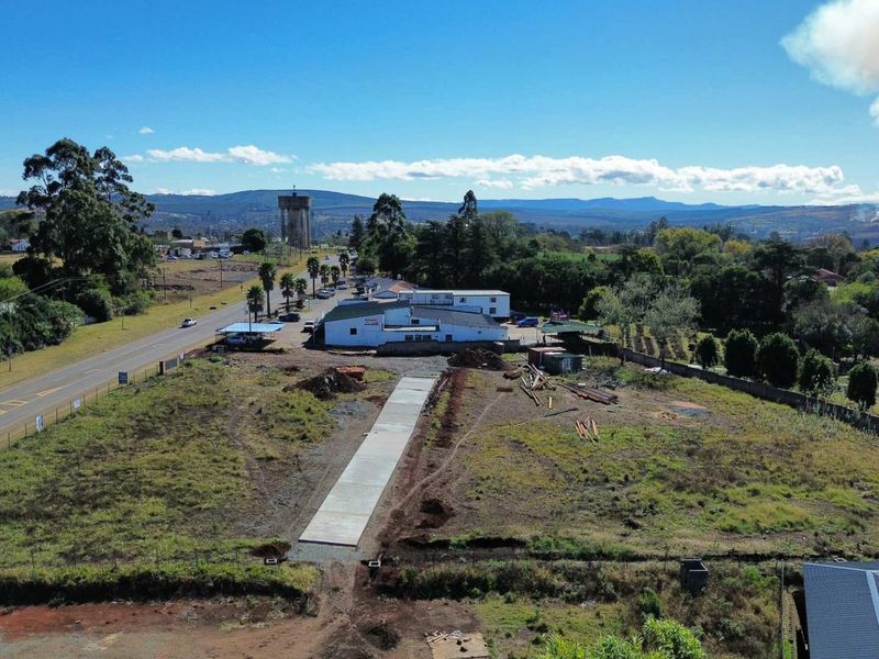 Aerial view of a vacant commercial land plot featuring a newly laid concrete driveway, perimeter fencing, and surrounding landscape.