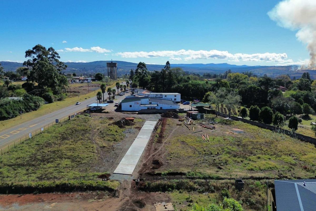 Aerial view of a vacant commercial land plot featuring a newly laid concrete driveway, perimeter fencing, and surrounding landscape.