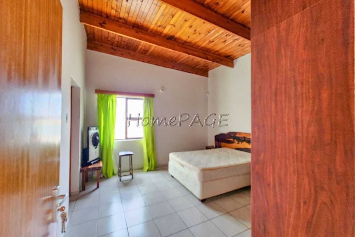 A bedroom featuring a high vaulted timber-beamed ceiling and tiled flooring, providing a spacious and rustic atmosphere.