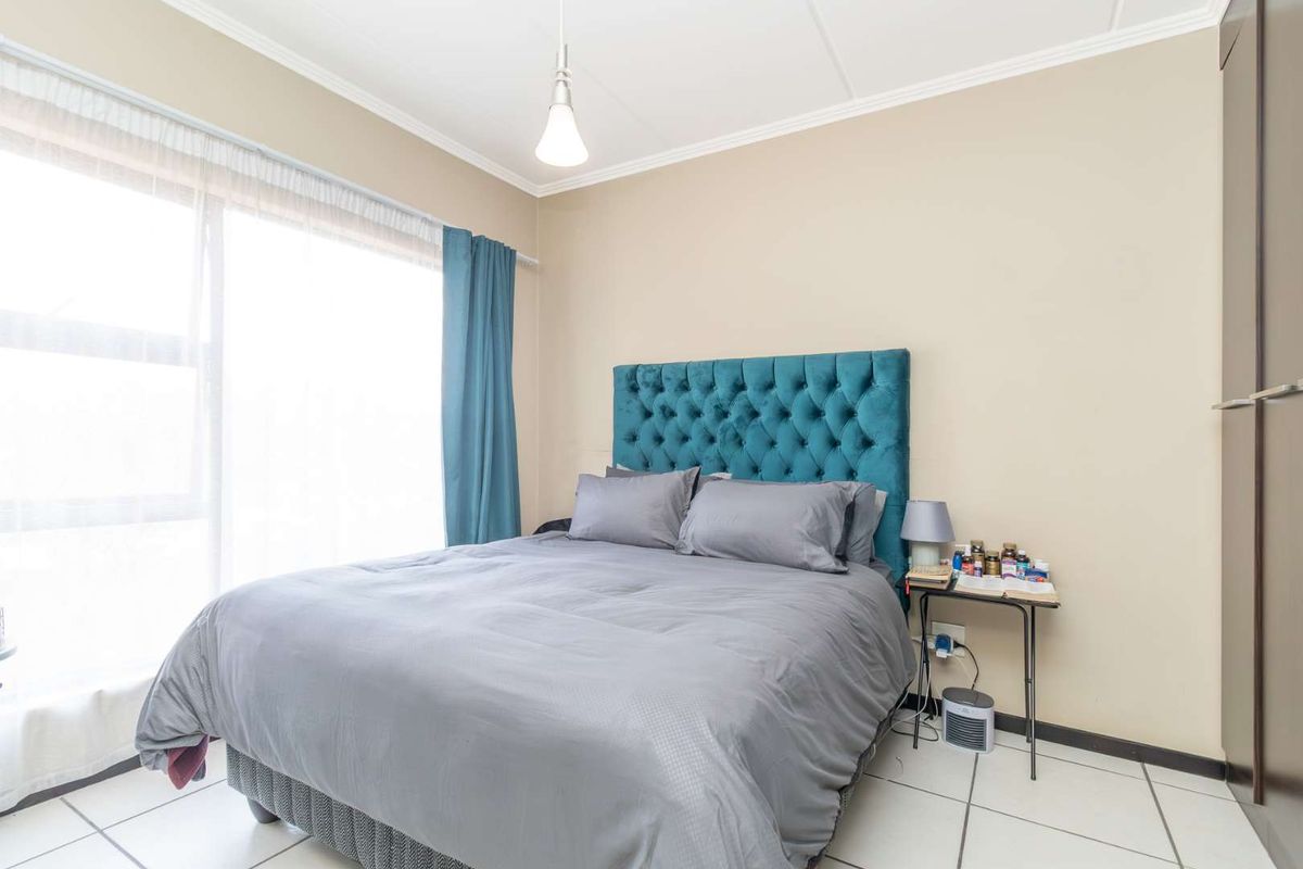 A well-lit bedroom featuring tiled flooring, a large sliding glass door providing natural light, and built-in cupboard storage.