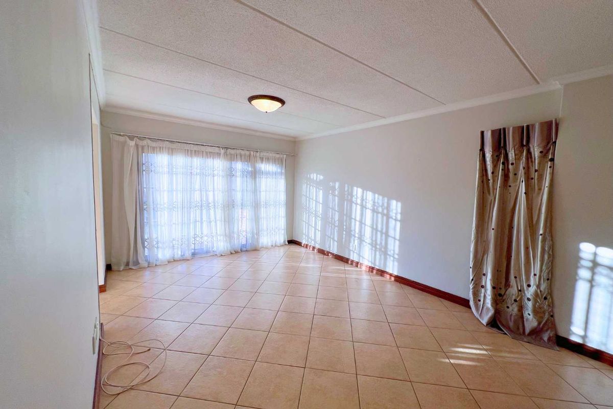 A bright and spacious living room featuring neutral floor tiles, a textured ceiling, and large sliding glass doors that provide ample natural light.