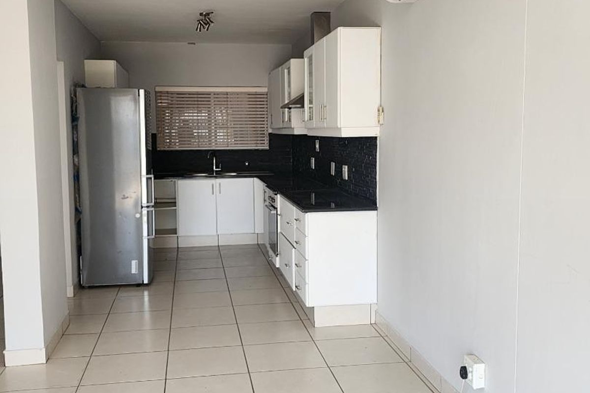 A clean, functional kitchen featuring white cabinetry, black granite countertops, integrated appliances, and tiled flooring, offering a bright and well-maintained workspace.