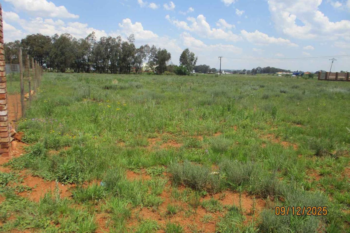 A view of a vacant residential plot featuring natural grass coverage, a wire boundary fence, and a brick pillar structure.