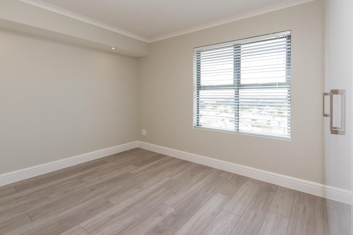 A bright and modern empty bedroom featuring light-toned laminate flooring, neutral walls, and a built-in cupboard with a window providing natural light.