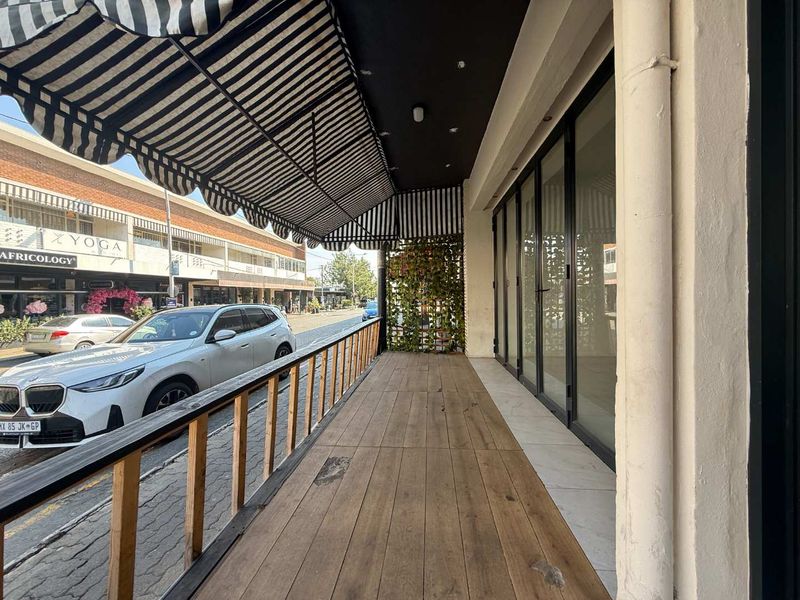 Covered outdoor patio area featuring timber decking, a striped awning, and bi-fold glass doors providing access to the retail space.