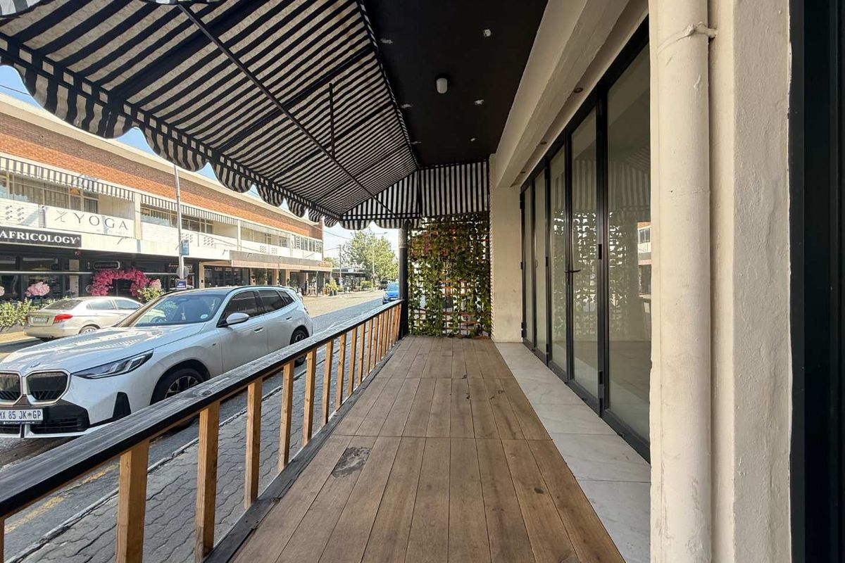 Covered outdoor patio area featuring timber decking, a striped awning, and bi-fold glass doors providing access to the retail space.