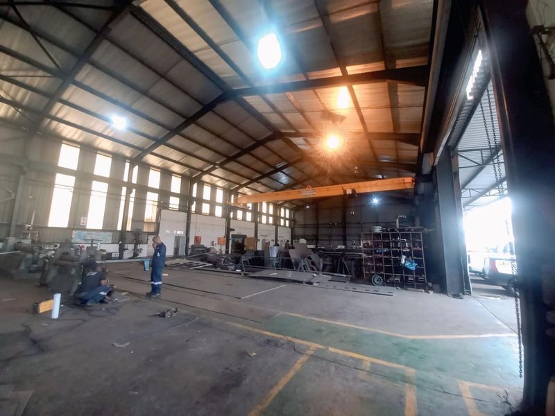 Spacious industrial warehouse featuring a high-clearance steel portal frame, overhead crane system, and large roller shutter access, suitable for heavy manufacturing or storage operations.