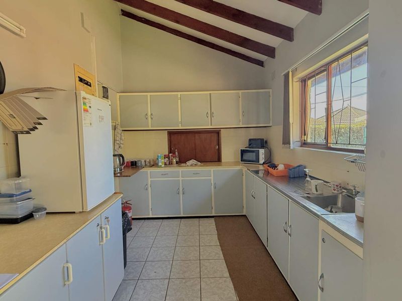 A dated kitchen featuring built-in cabinetry, laminate countertops, a stainless steel sink, and exposed timber ceiling beams with a vaulted ceiling.