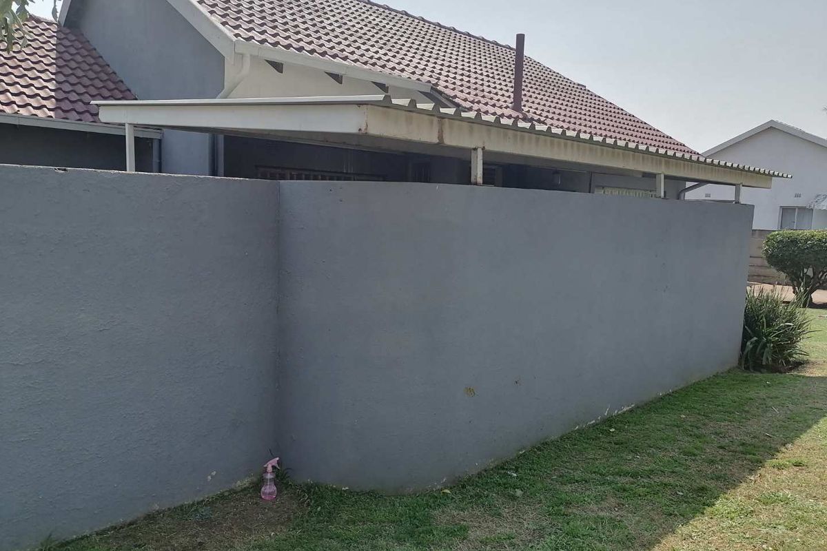 Rear view of the property featuring a tiled roof, a boundary wall, and a covered patio area with metal roofing.