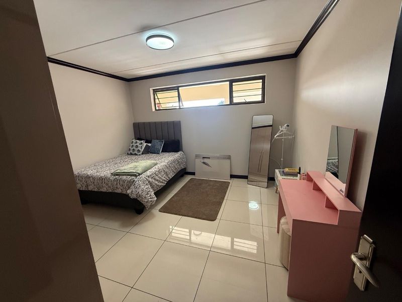 A bedroom featuring tiled flooring, neutral wall finishes, and horizontal louvre windows providing natural light.