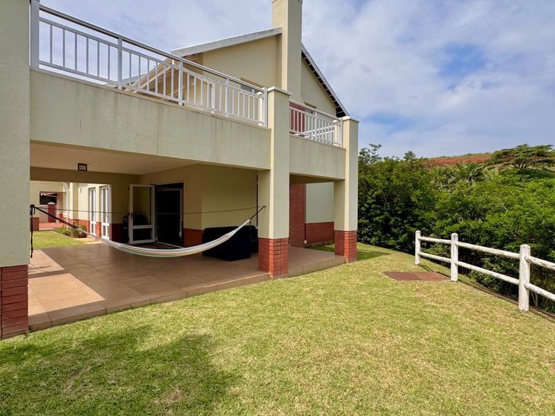 A spacious covered patio area with tiled flooring and brick pillars, leading out to a private lawn and garden with scenic views.
