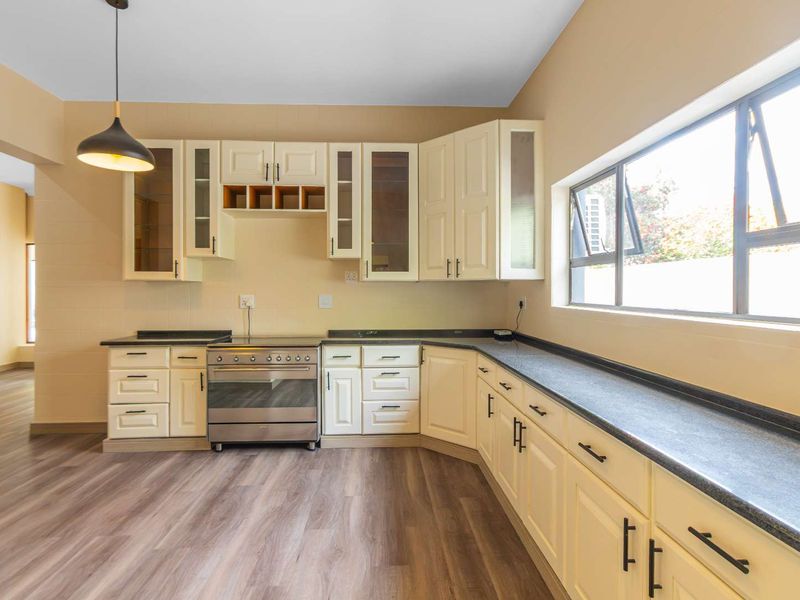 A clean, well-lit kitchen featuring cream-colored cabinetry, dark laminate countertops, a stainless steel stove, and modern wood-look laminate flooring.