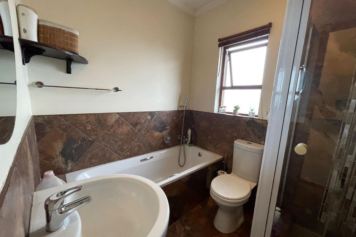 A functional bathroom featuring a bathtub, separate shower enclosure, pedestal basin, and toilet with brown tiled splashbacks and flooring.