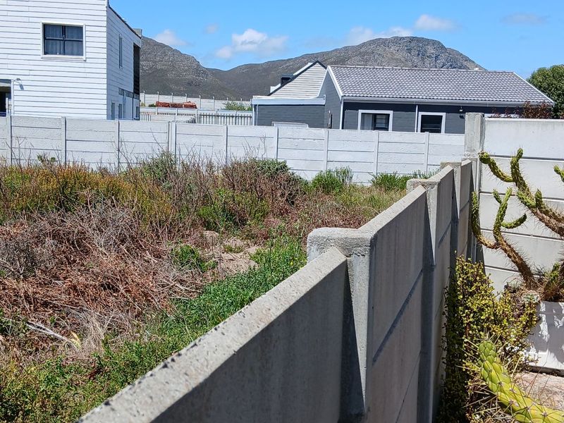 A vacant residential plot featuring a precast concrete boundary wall and natural, overgrown vegetation with mountain views in the background.
