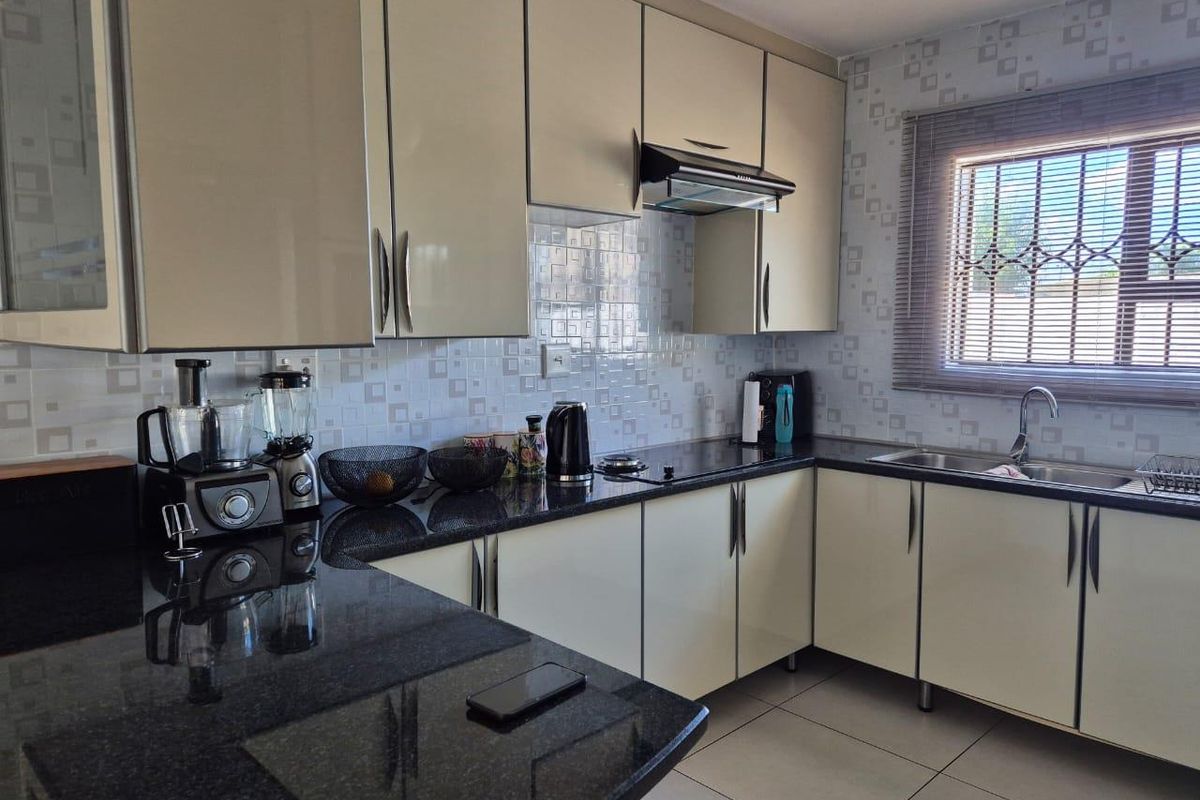 Modern kitchen featuring high-gloss cabinetry, dark granite countertops, tiled backsplash, and a stainless steel sink with a window view.