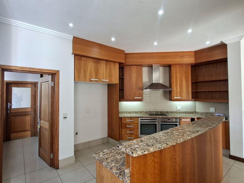A spacious kitchen featuring wooden cabinetry, granite countertops, a breakfast bar, and built-in double oven with extractor fan, finished with tiled flooring.