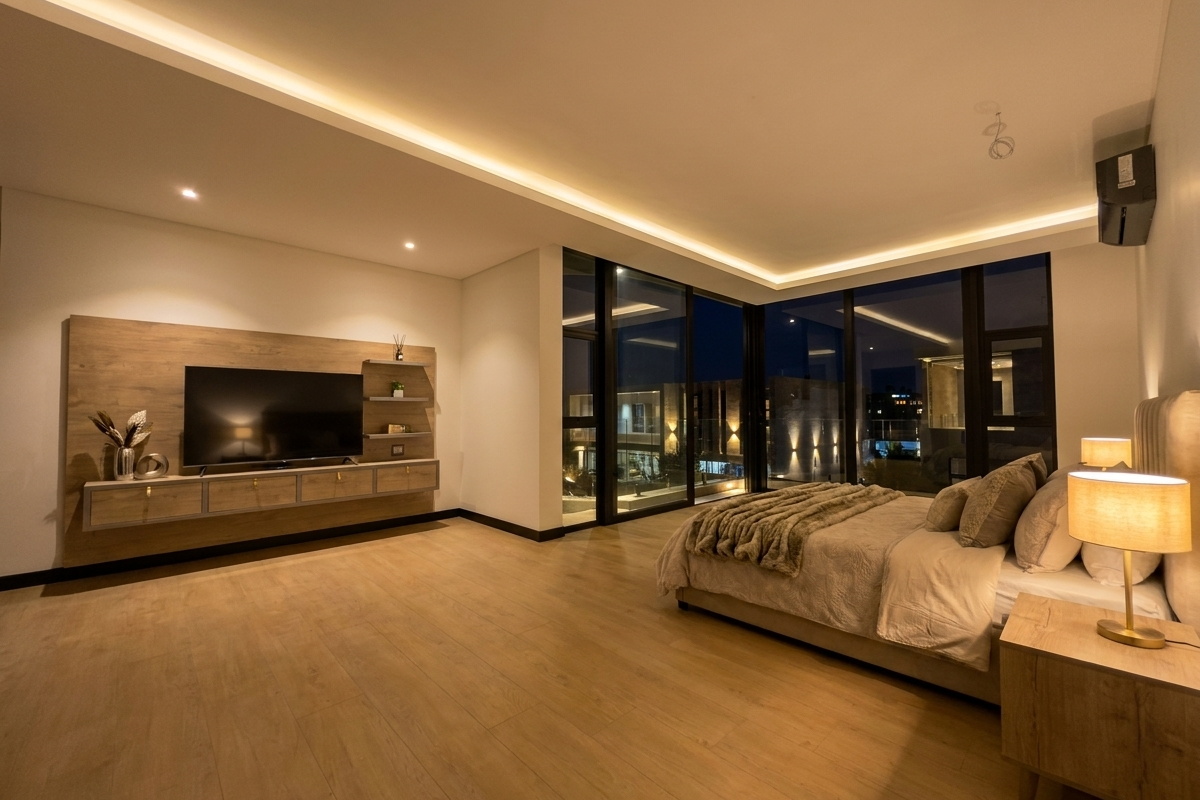 Modern bedroom featuring floor-to-ceiling windows, recessed LED ceiling lighting, and a custom built-in wooden media console with integrated shelving.