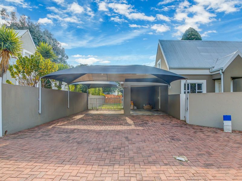 A paved driveway featuring a modern shade cloth carport structure, enclosed by boundary walls, providing convenient off-street parking.