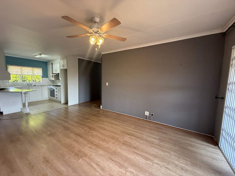 An open-plan living and kitchen area featuring laminate flooring, a ceiling fan, and a functional kitchen layout with built-in cabinetry and appliances.
