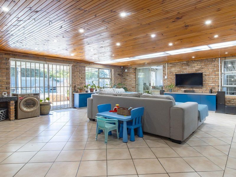 Spacious open-plan living area featuring exposed brick walls, a warm timber ceiling, ceramic tiled flooring, and direct access to the outdoor patio area.