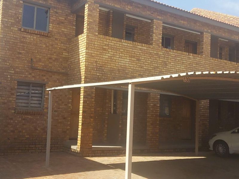 Exterior view of a multi-story face brick apartment building featuring a covered carport and paved driveway area.