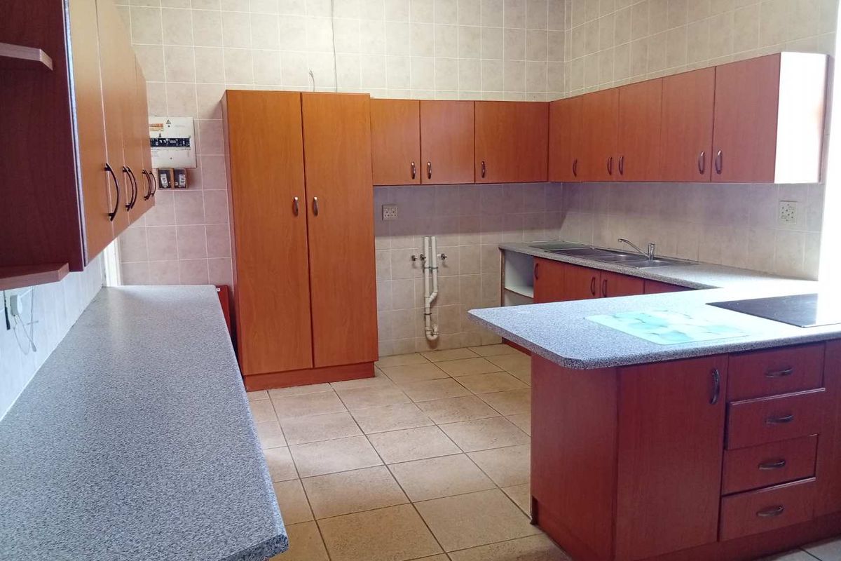 A functional kitchen featuring extensive laminate cabinetry, ample countertop space, a double sink, and tiled finishes throughout.