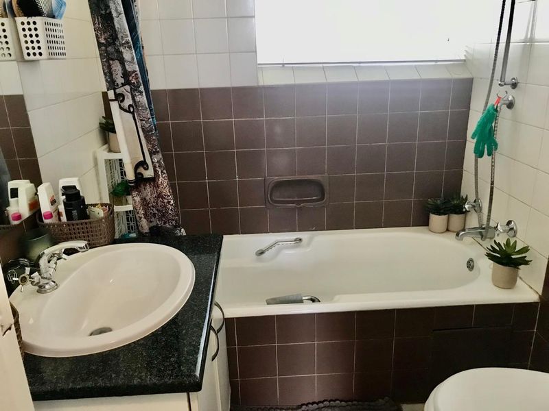 A functional bathroom featuring a built-in bathtub, vanity sink with granite countertop, and tiled wall finishes.