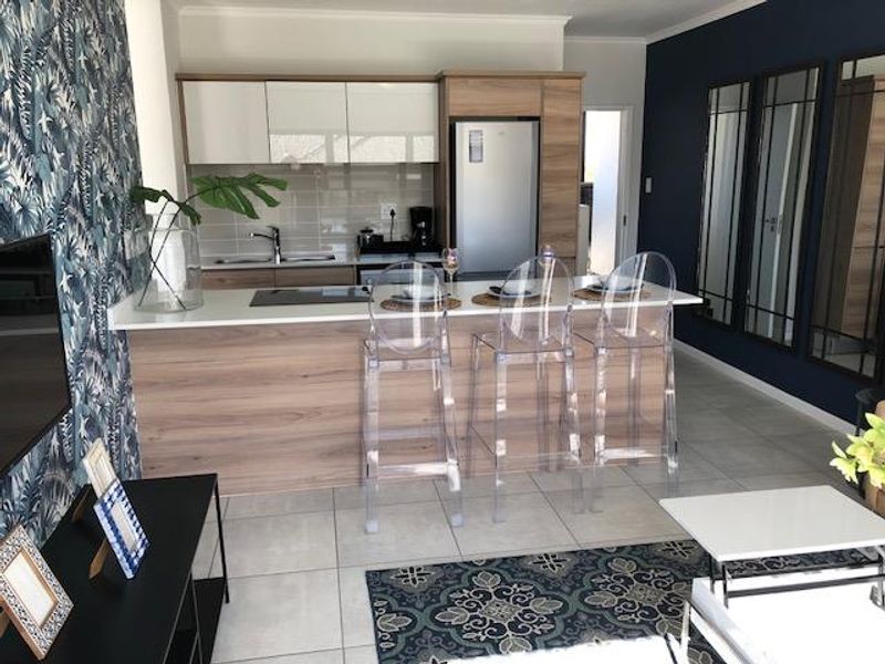 Modern open-plan kitchen featuring wood-grain cabinetry, stone countertops, and a breakfast island, seamlessly integrated with the living area and stylish mirrored wall accents.